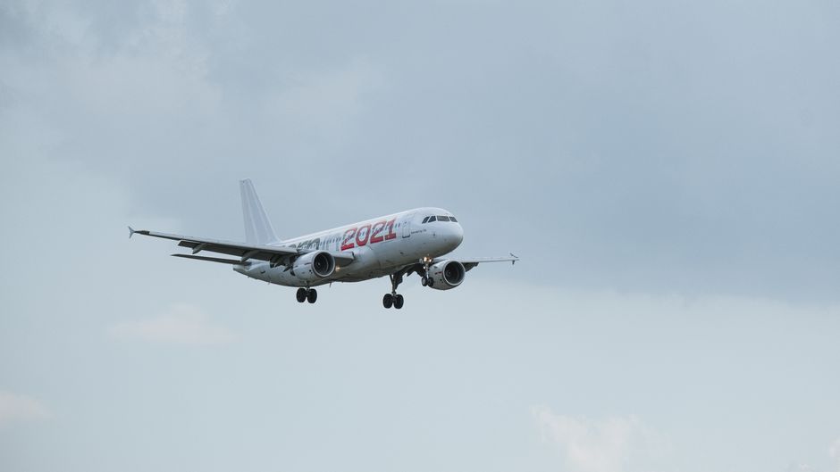 An Airbus A320 airplane with '2021' livery captured in mid-air against a cloudy sky.