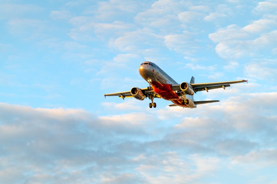 A low-angle view of a passenger airplane flying amidst clouds in a clear blue sky.
