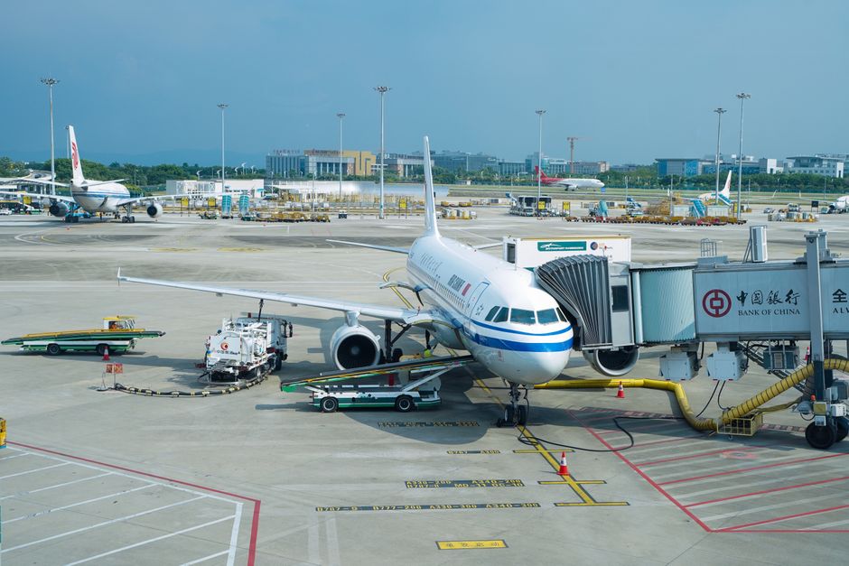Airplane parked at a terminal gate with boarding bridge in a bustling airport.
