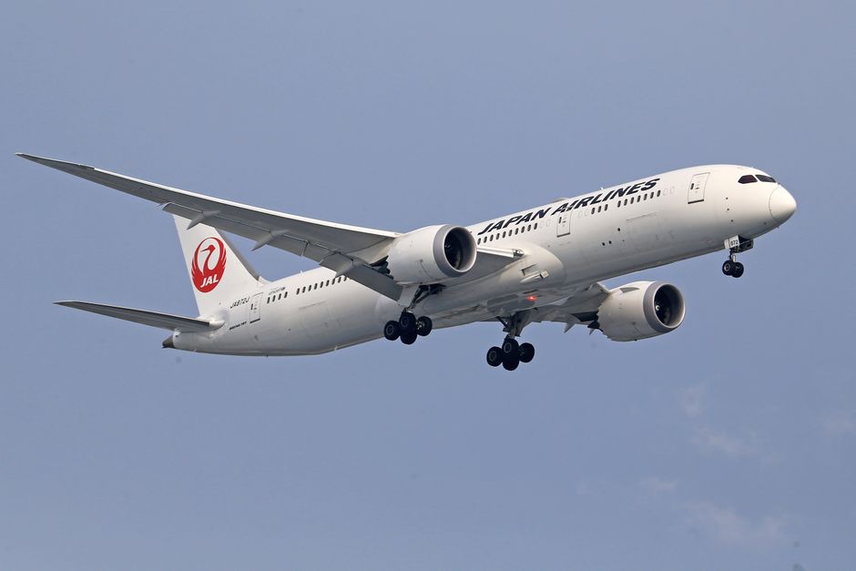 Japan Airlines aircraft in mid-air flight during the day with landing gear extended.