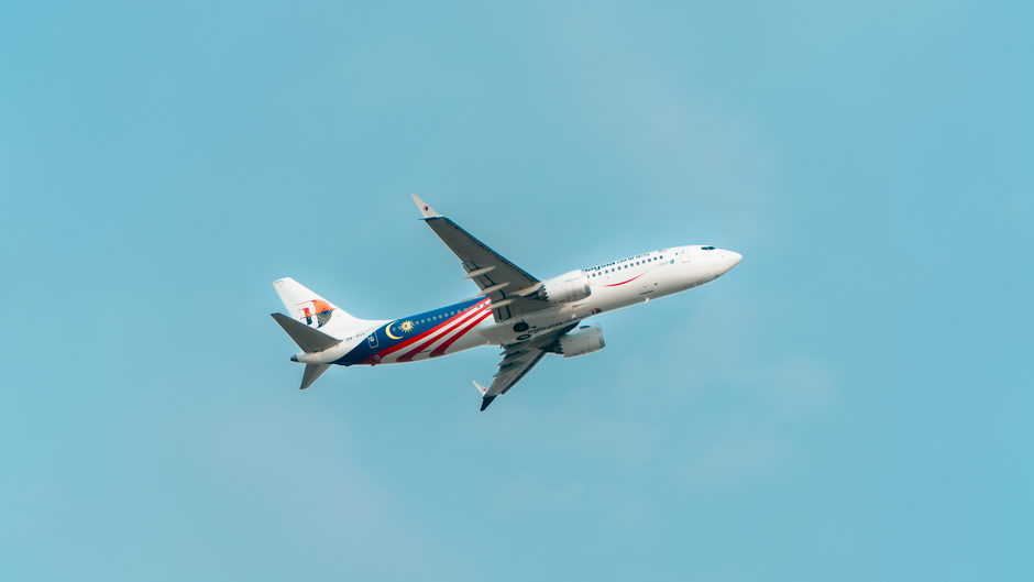 A commercial airplane featuring the Malaysian flag design flying in a clear blue sky.