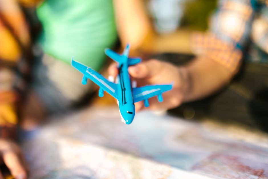 Close-up of a blue toy airplane held over a colorful map with blurred background.