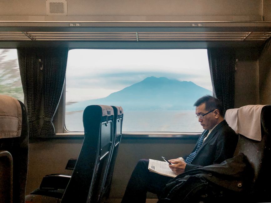 A man sitting on a train reads while Mount Fuji is visible through the window.